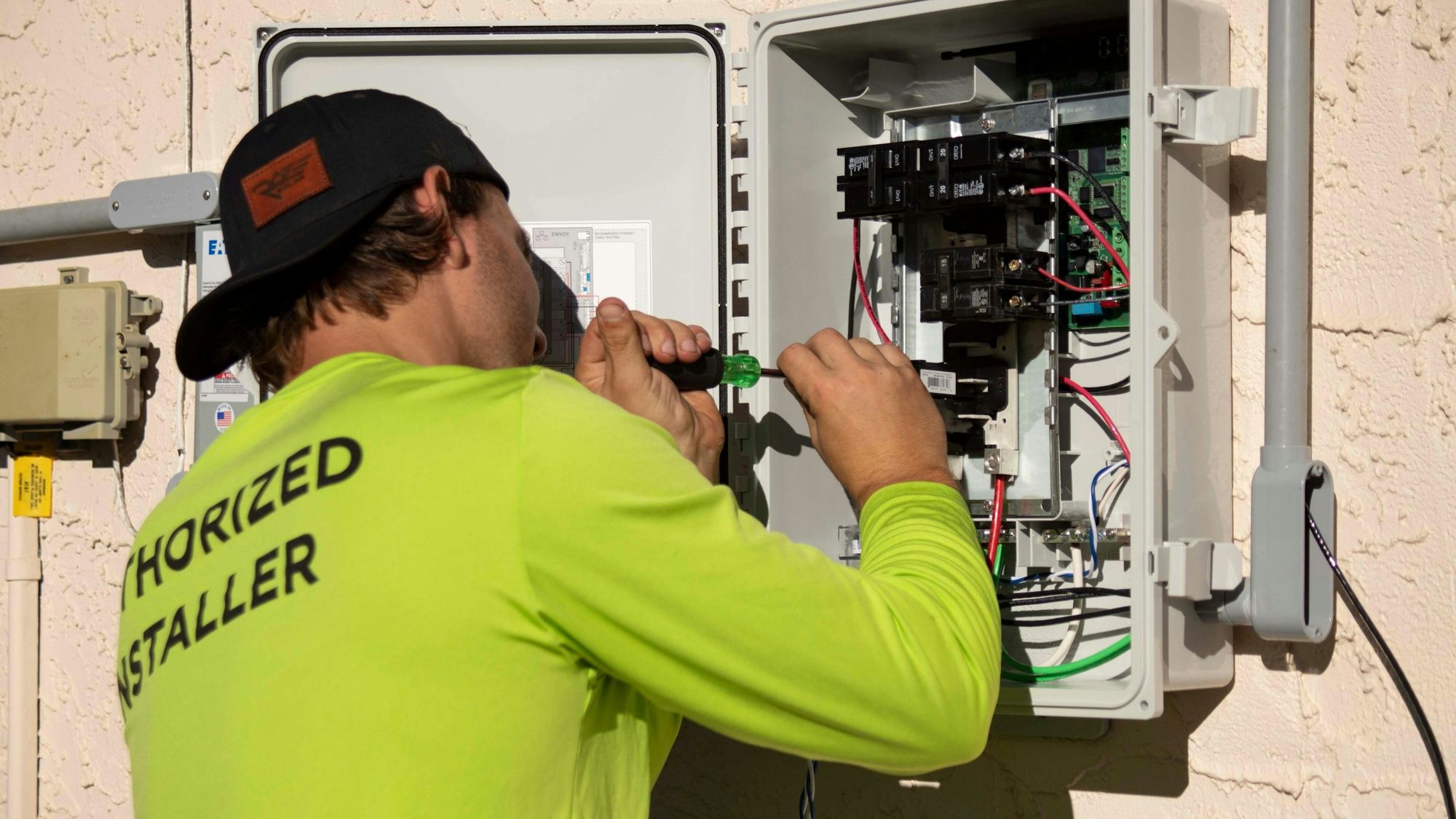 An electrician in a hi-vis top working on an open electrical panel